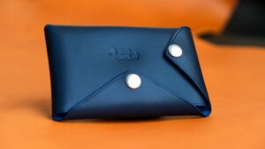 Sleek blue leather wallet with snap closures against a vibrant orange background. Perfect for minimalist style.